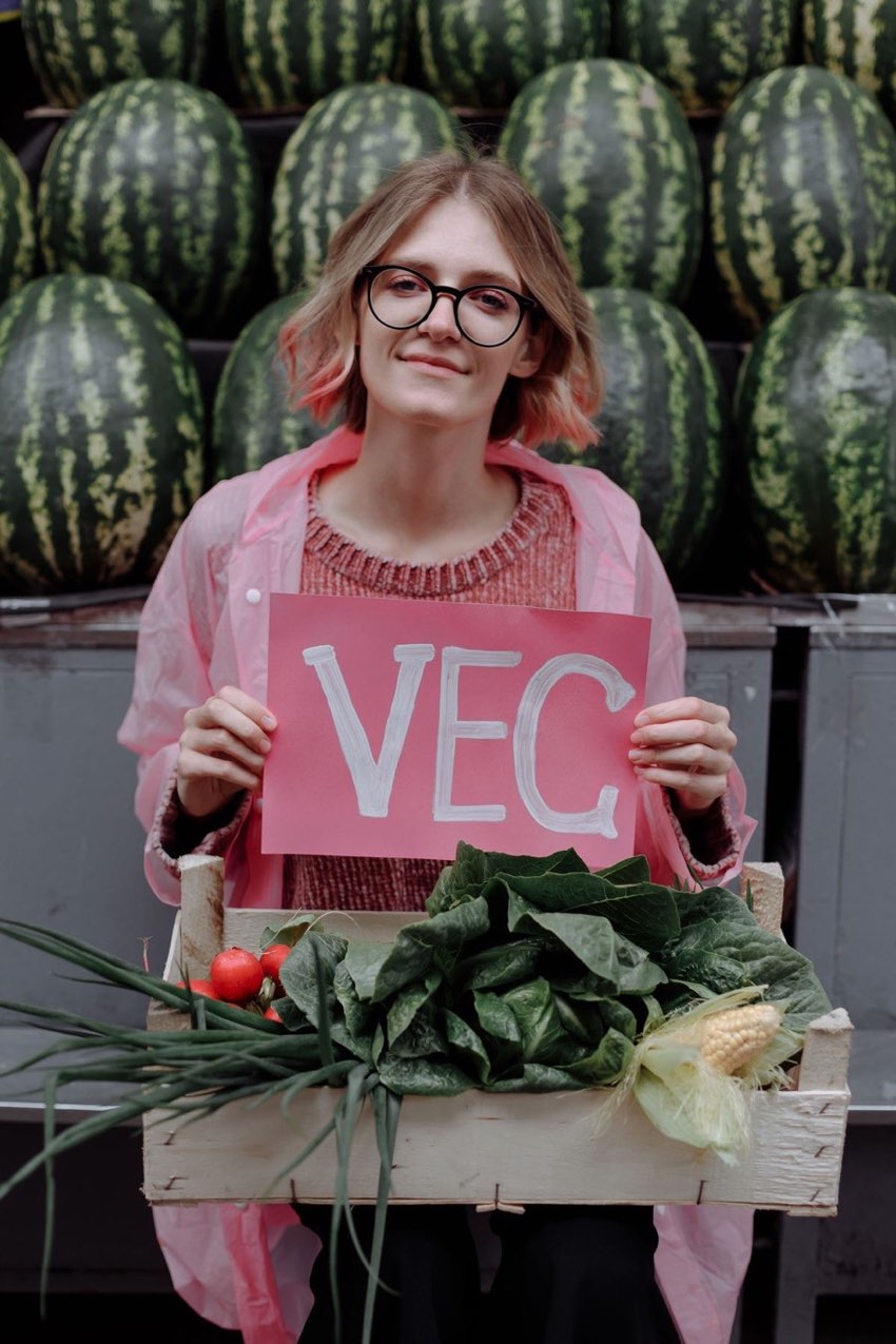 Illustrative stock photograph showing a person holding a sign reading VEG in front of a market stall